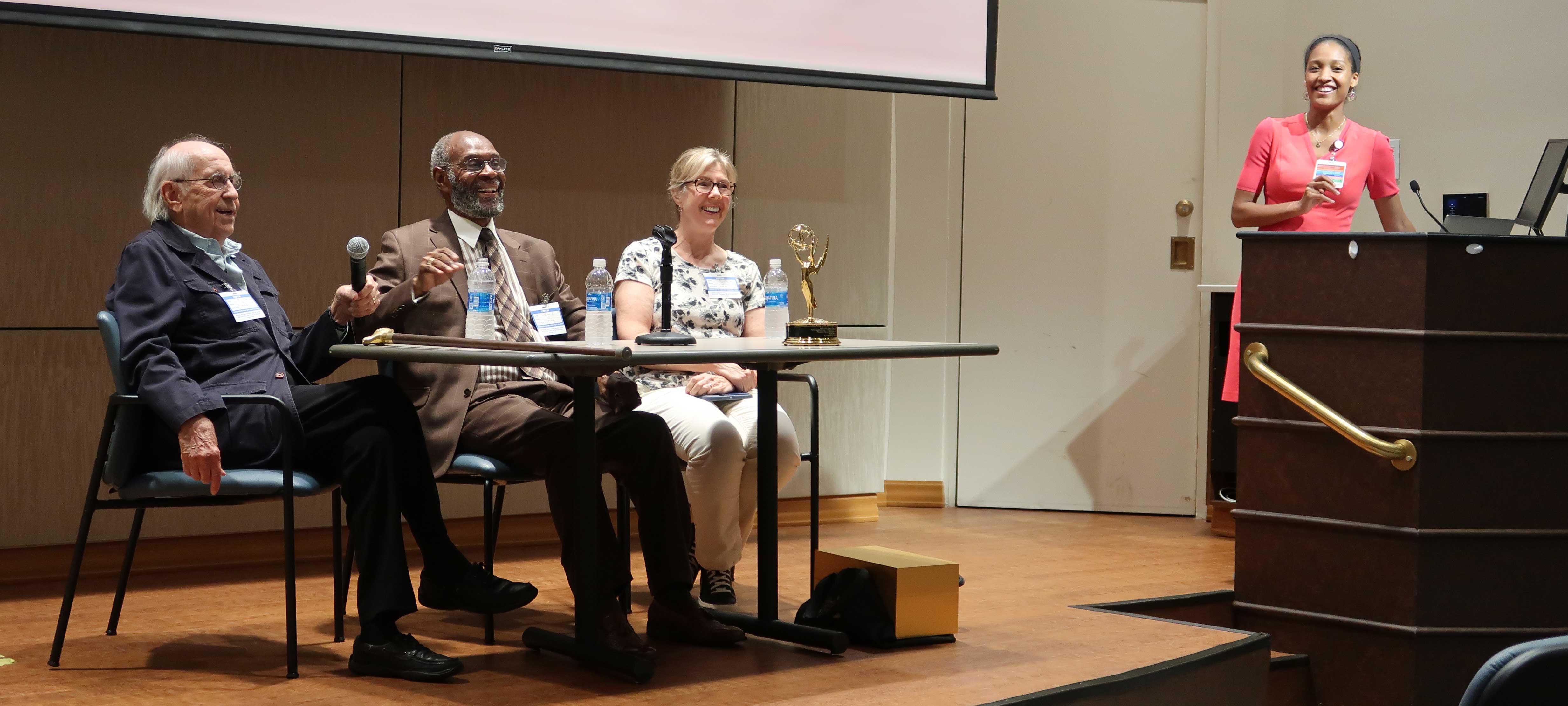 Panelists sitting at a table smiling in response to applause